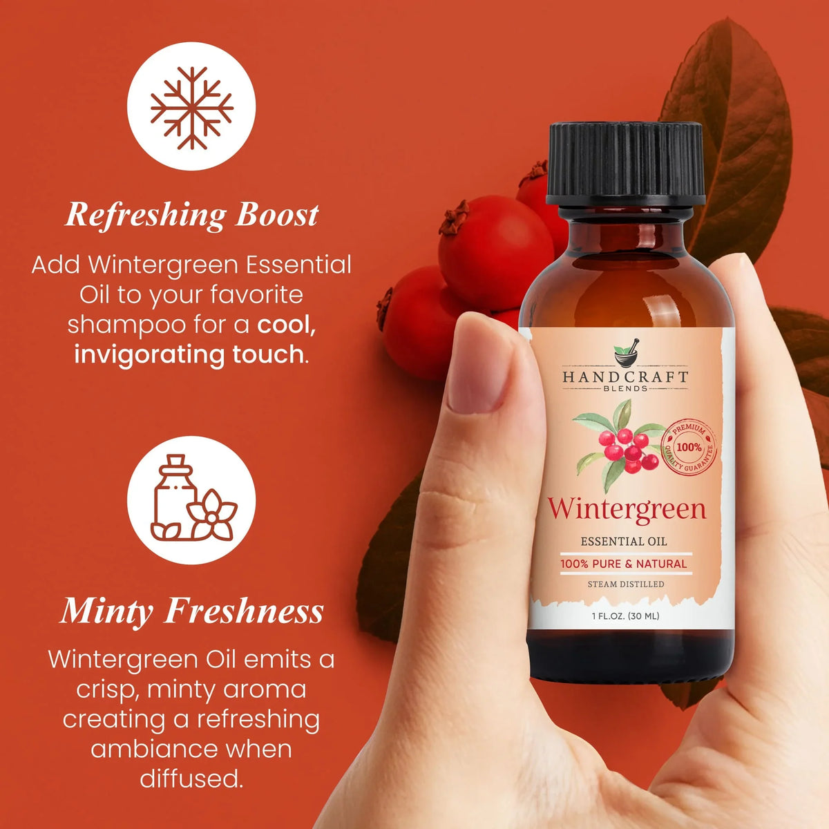 Hand holding a bottle of wintergreen essential oil with berries and leaves on an orange background