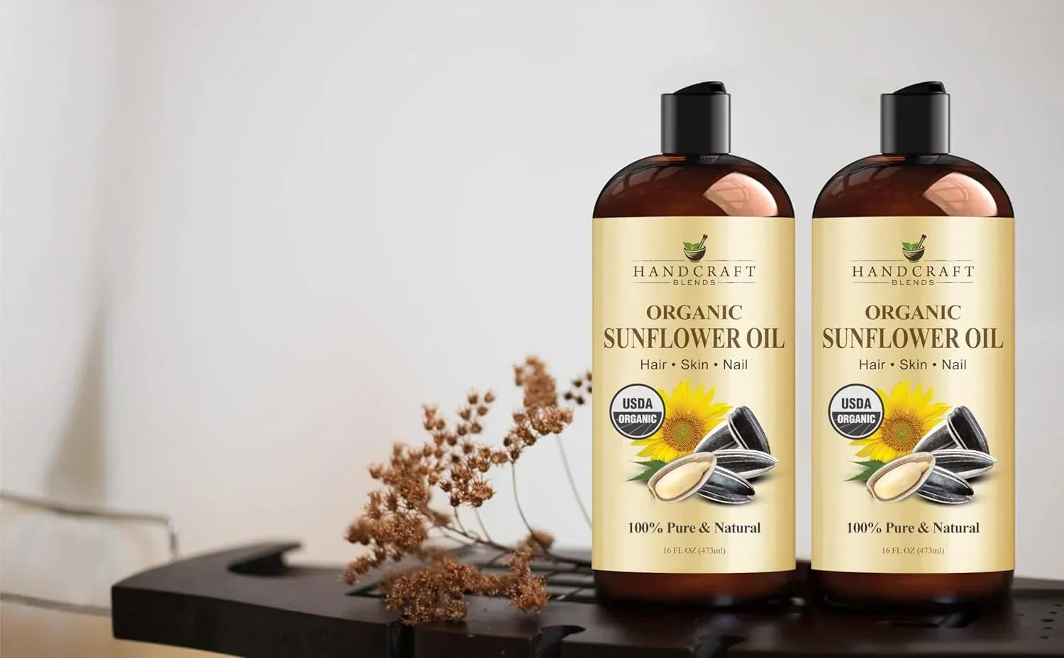 Two bottles of organic sunflower oil for hair, skin, and nails on a table with dried flowers.