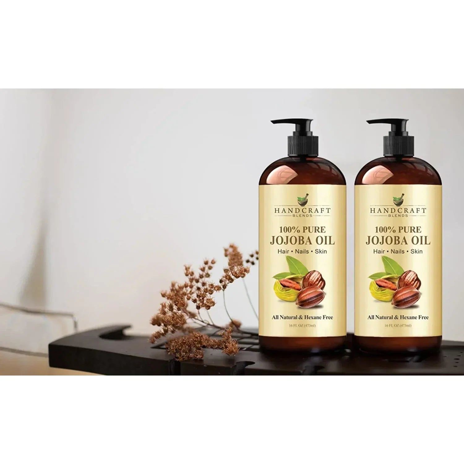 Two bottles of 100% pure jojoba oil for hair, nails, and skin on a table with dried flowers