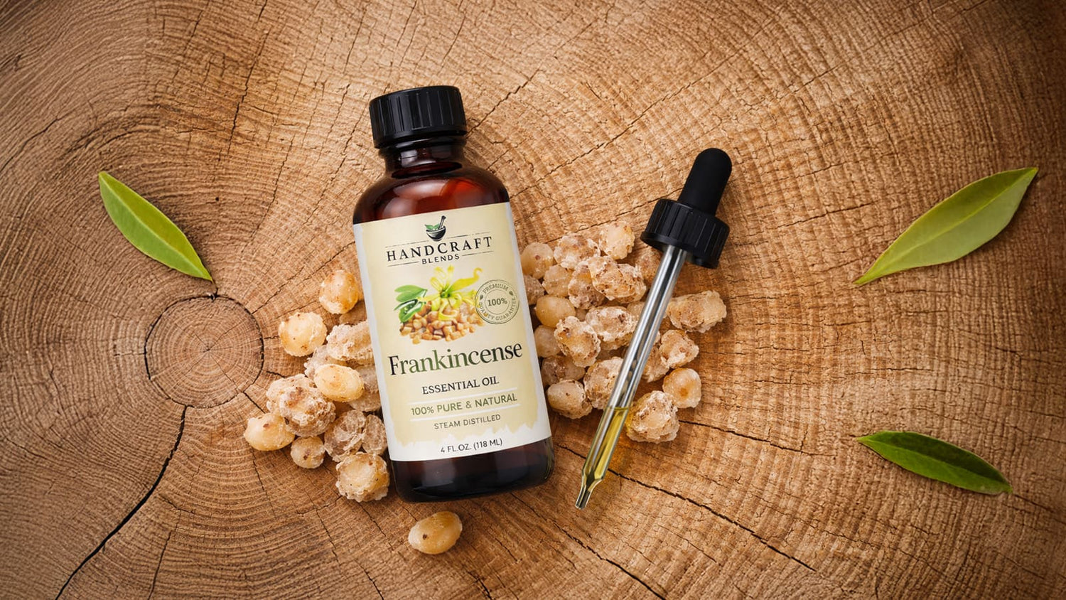 Frankincense essential oil bottle with dropper, resin, and green leaves on wood background