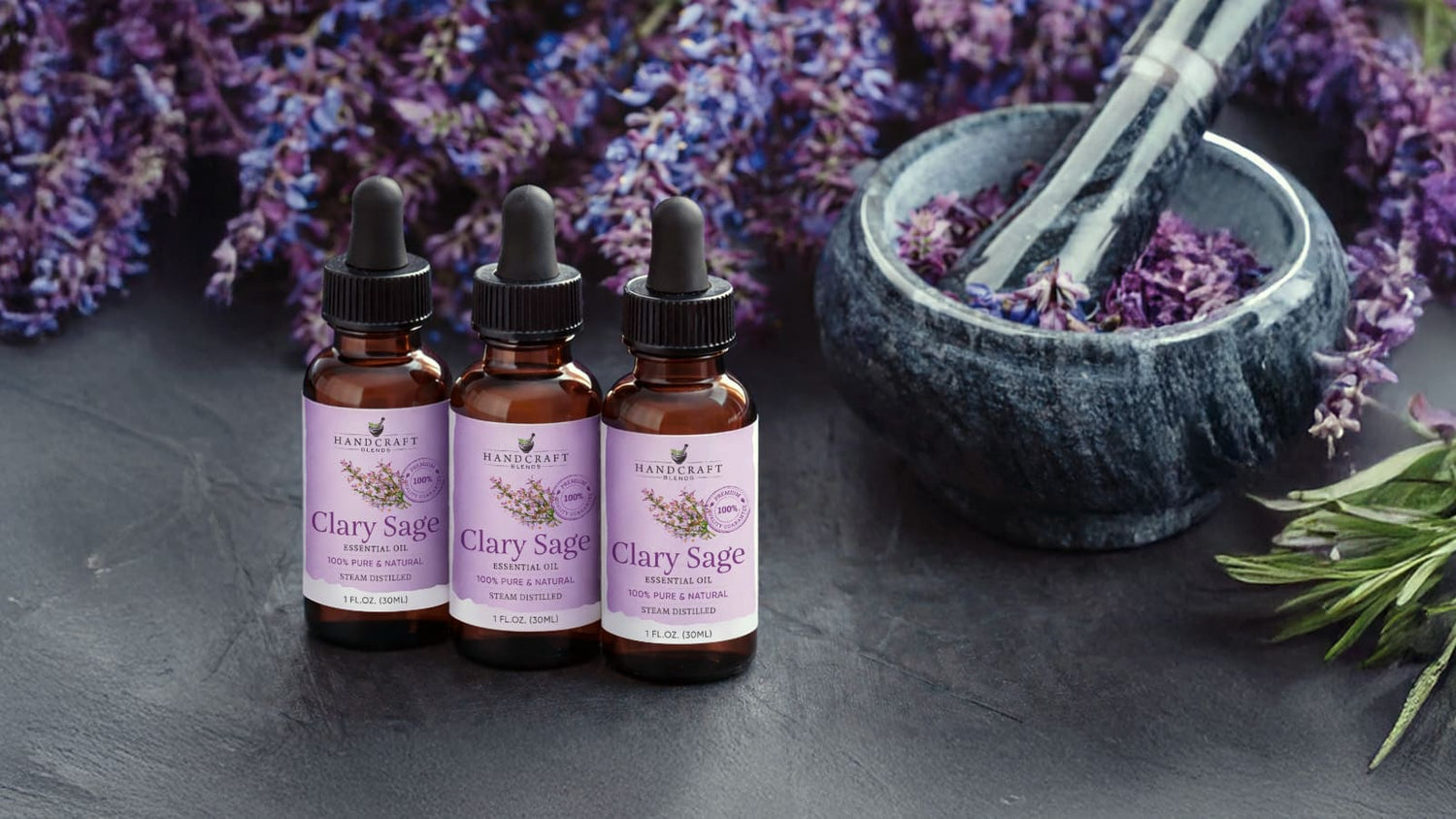 Clary sage essential oil bottles with dried clary sage flowers and mortar on dark background