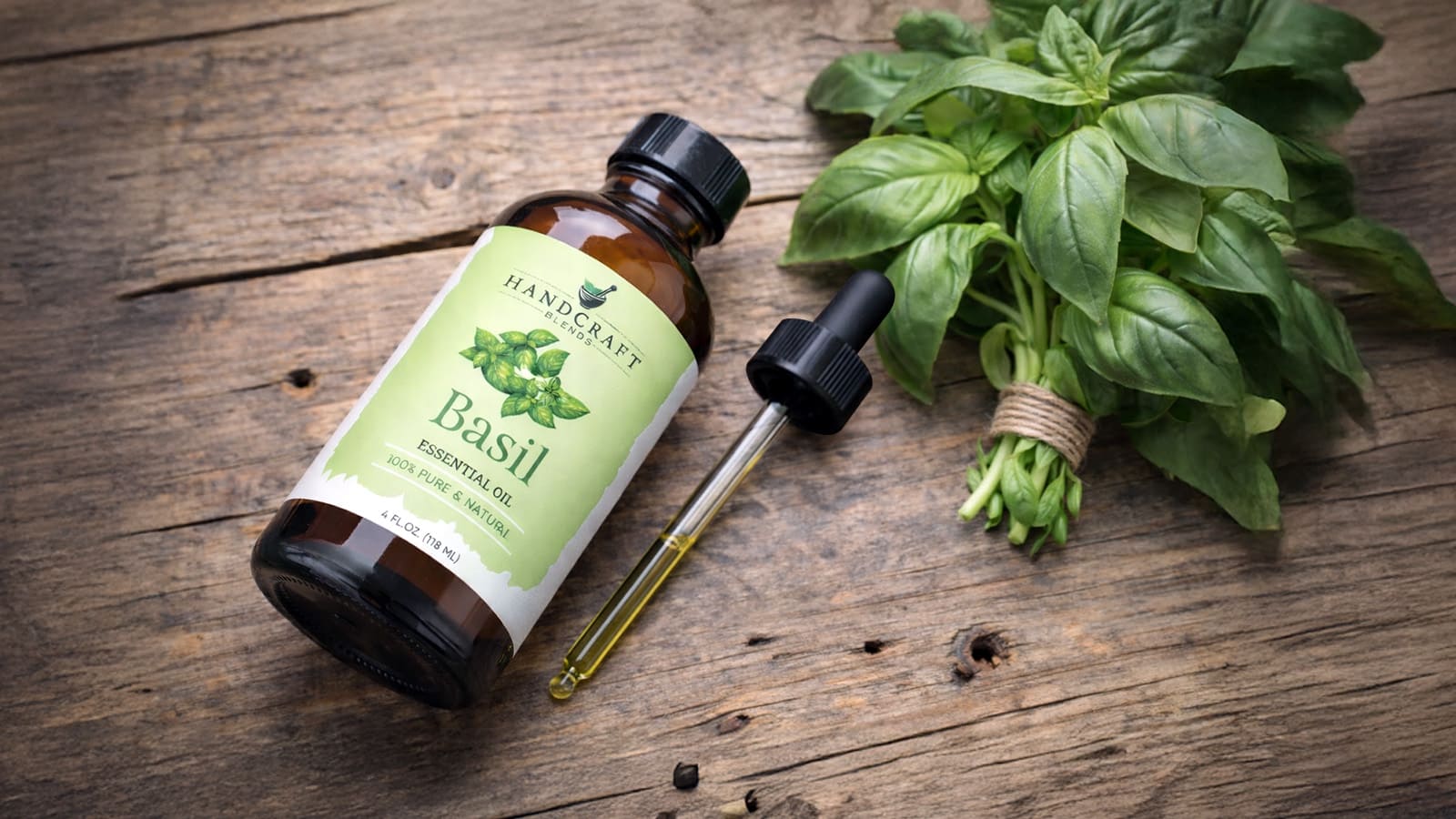 Basil essential oil bottle with dropper and fresh basil leaves on rustic wooden table
