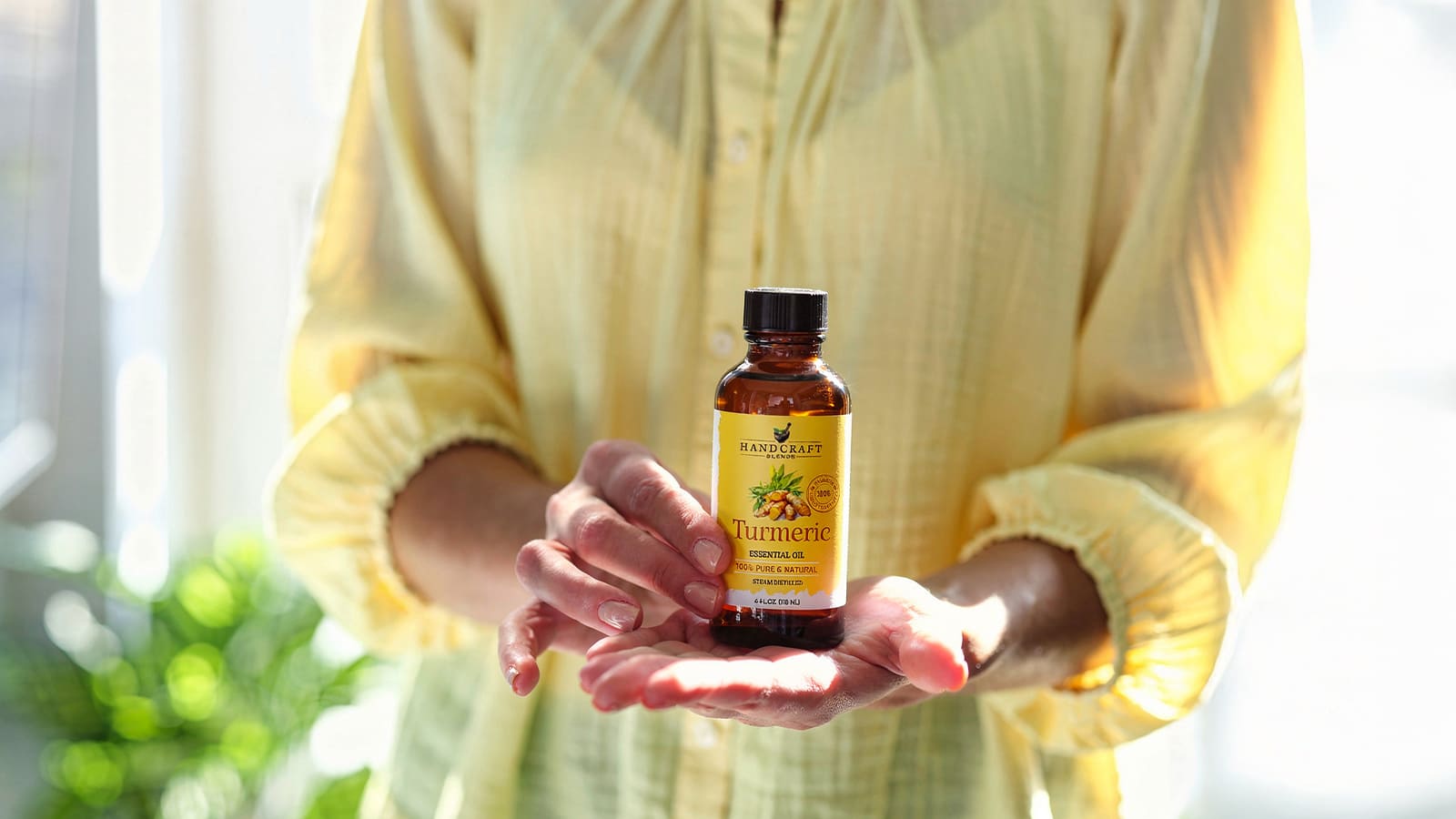 Person holding a bottle of turmeric essential oil, natural aromatherapy product