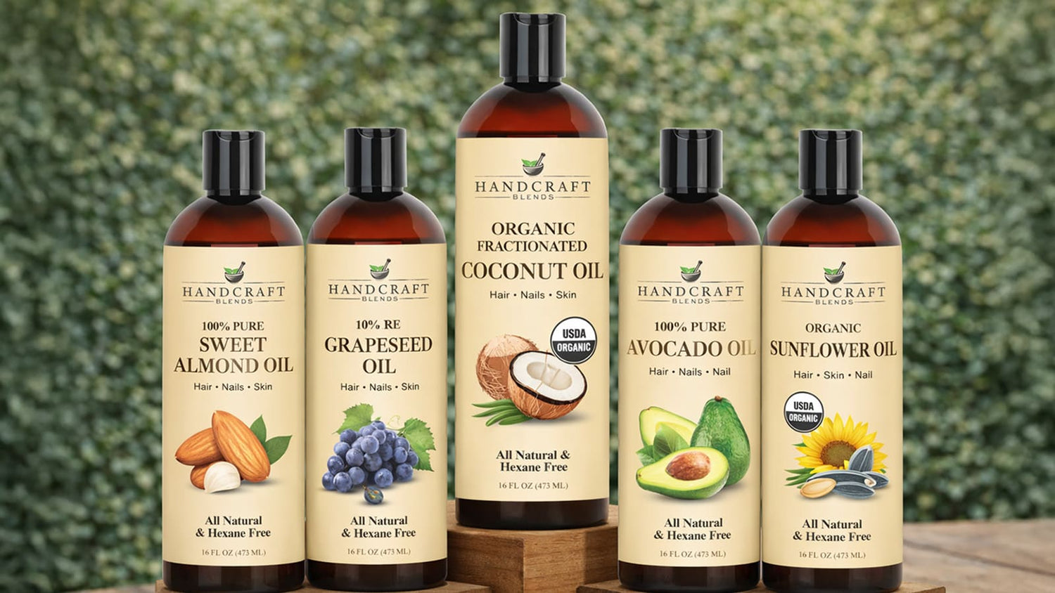 Five bottles of carrier oils including sweet almond, grapeseed, coconut, avocado, and sunflower oil on a wooden surface outdoors.