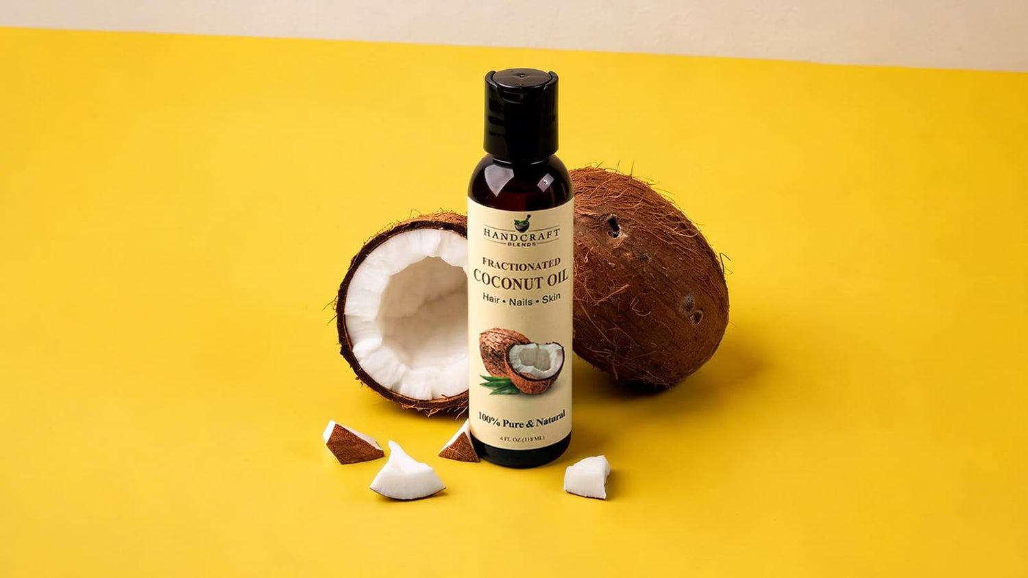 Fractionated coconut oil bottle with fresh coconut pieces on yellow background