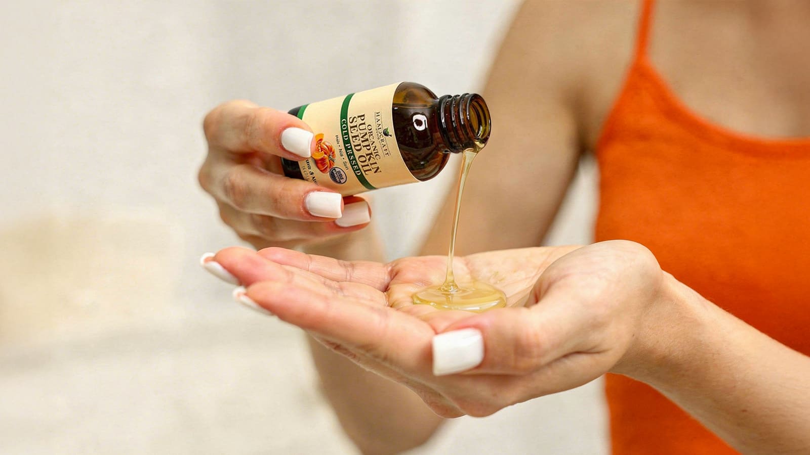 Woman pouring cold pressed pumpkin seed oil from bottle into hand, natural skincare
