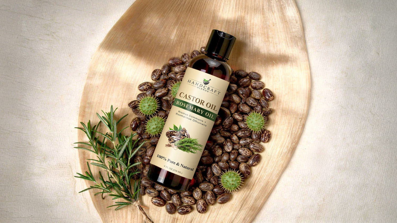 Bottle of castor oil with rosemary oil on wooden tray, surrounded by castor beans and rosemary sprig