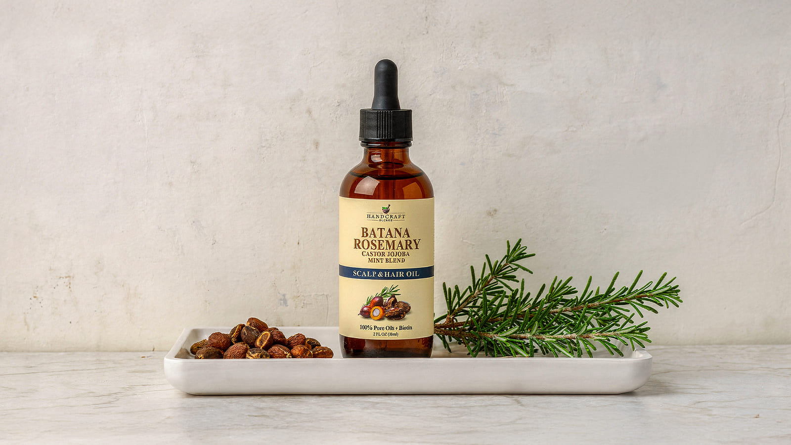 Batana rosemary scalp and hair oil bottle with nuts and rosemary sprig on a tray