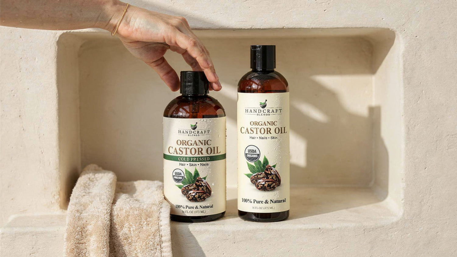 Two bottles of organic castor oil for hair, skin, and nails on a beige shelf with a towel.