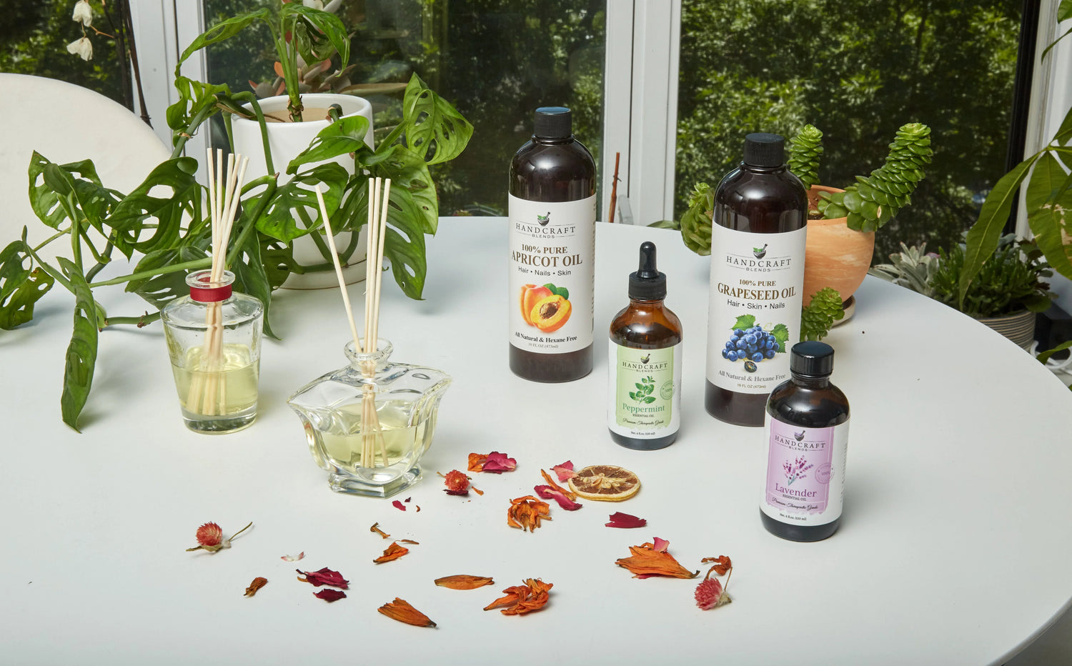 Handcraft Blends essential oils and carrier oils on a white table with diffuser sticks and plants